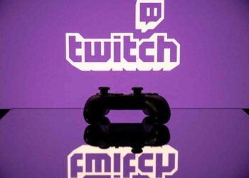یک کنترلر بازی مشکی که در مقابل لوگوی بنفش Twitch قرار دارد و روی یک سطح براق منعکس شده است.