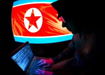 نمایی از فردی که با لپ‌تاپ‌اش دارد کد نویسی می‌کند و در پس‌زمینه پرچم آمریکای شمالی قرار گرفته