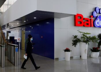 ورودی ساختمان Baidu با پله‌های چوبی، گیت‌های ورودی و لوگوی قرمز و آبی بزرگ Baidu روی دیوار، در حالی که یک کارمند در پیش‌زمینه در حال راه رفتن است.