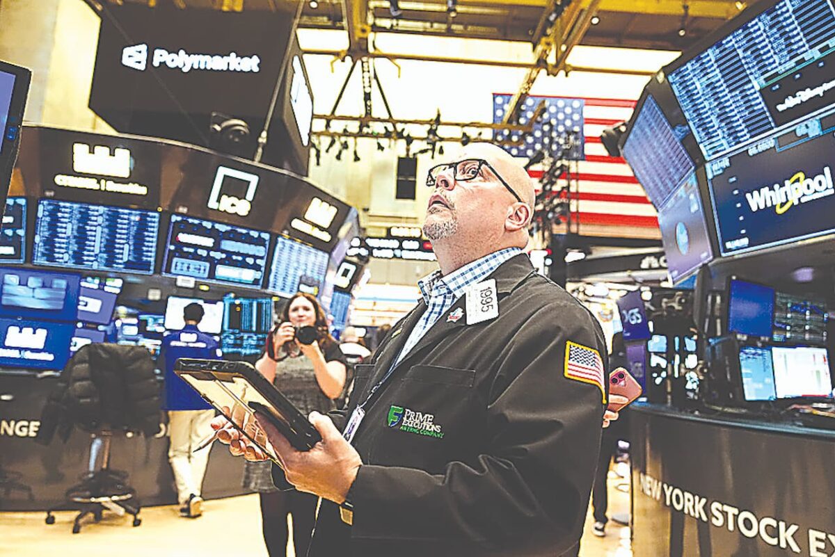 کارگزار بورس (Stock Broker) در حال بررسی یک تبلت در طبقه بورس نیویورک (NYSE) با چندین صفحه نمایش اطلاعاتی و پرچم آمریکا در پس‌زمینه.