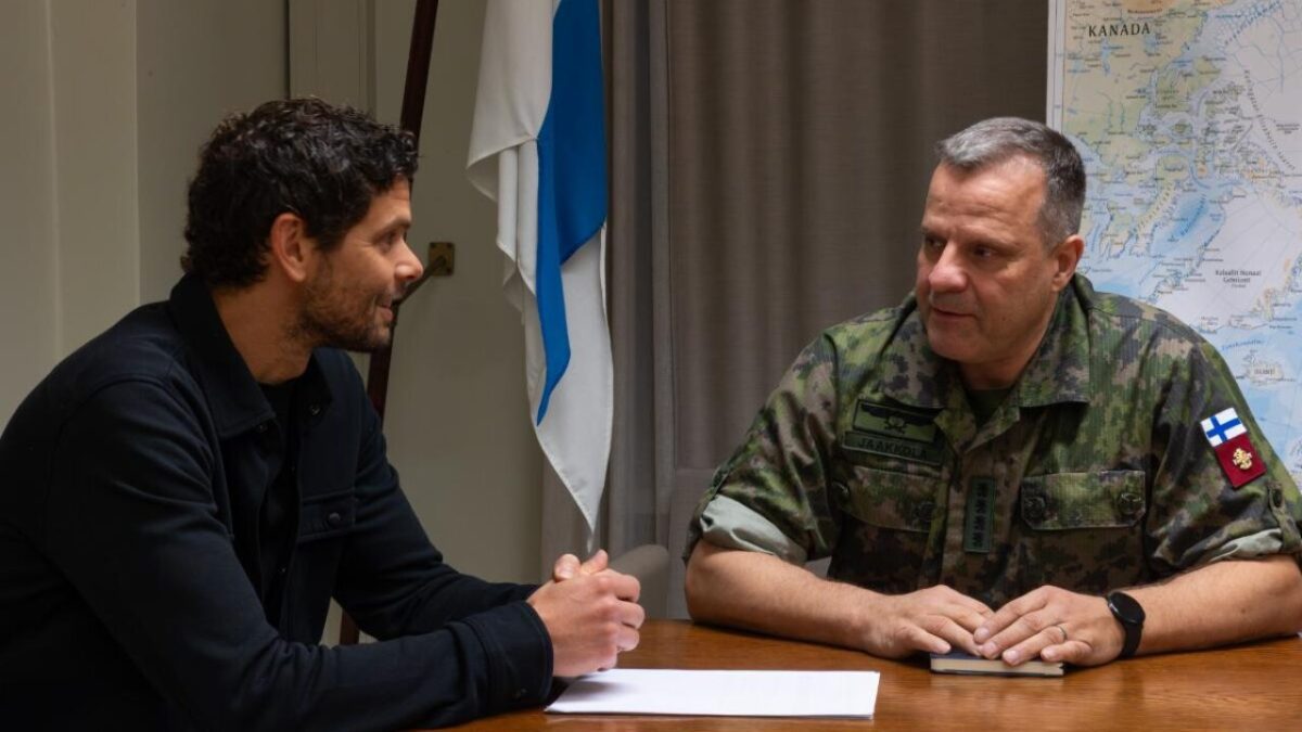 یک مرد (احتمالاً مدیرعامل NestAI) در حال صحبت با یک افسر نظامی فنلاندی در یک میز، با پرچم فنلاند در پس‌زمینه.