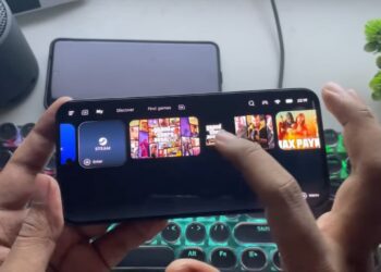 یک فرد در حال استفاده از برنامه GameHub بر روی یک گوشی هوشمند در حالت افقی، که بازی‌هایی مانند Grand Theft Auto و Max Payne را در حال استریم یا اجرا نمایش می‌دهد و یک کیبورد مکانیکی روشن در پس‌زمینه دیده می‌شود.