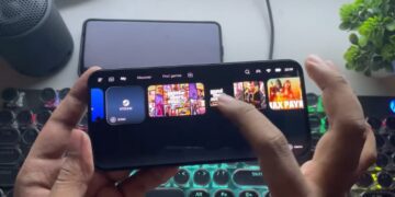 یک فرد در حال استفاده از برنامه GameHub بر روی یک گوشی هوشمند در حالت افقی، که بازیهایی مانند Grand Theft Auto و Max Payne را در حال استریم یا اجرا نمایش میدهد و یک کیبورد مکانیکی روشن در پسزمینه دیده میشود.