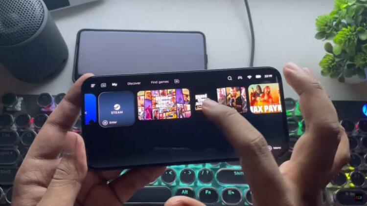 یک فرد در حال استفاده از برنامه GameHub بر روی یک گوشی هوشمند در حالت افقی، که بازیهایی مانند Grand Theft Auto و Max Payne را در حال استریم یا اجرا نمایش میدهد و یک کیبورد مکانیکی روشن در پسزمینه دیده میشود.