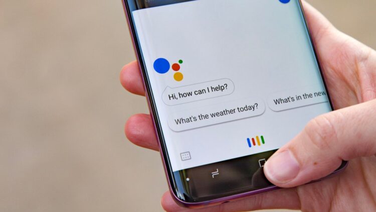 یک گوشی هوشمند که برنامه Google Assistant روی صفحه آن باز است و حباب‌های گفتاری "Hi, how can I help?" و "What's the weather today?" دیده می‌شوند.