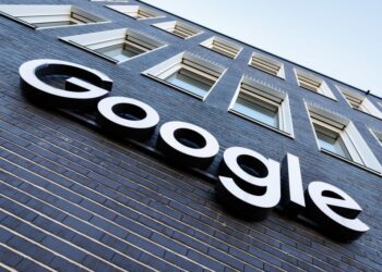 نمای بیرونی یک ساختمان آجری تیره با پنجره‌های سفید، که لوگوی برجسته و سفید "Google" بر روی آن نصب شده است.