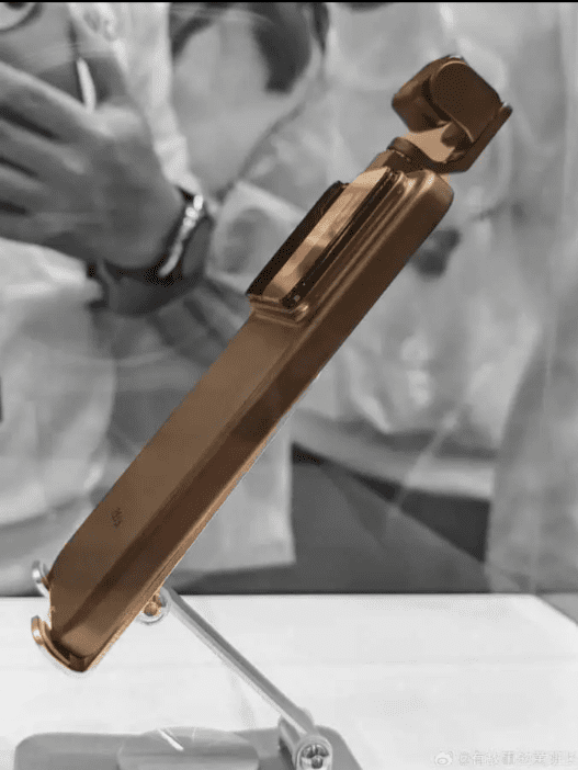 یک گوشی هوشمند طلایی رنگ Honor با ماژول دوربین بزرگ و جداگانه در بالا که به صورت عمودی روی یک پایه کوچک نمایش داده شده است.