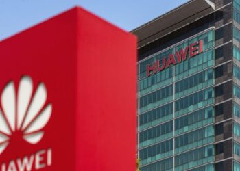 ساختمان اداری هواوی با لوگوی قرمز Huawei روی شیشهها و یک ماکت لوگوی بزرگ قرمز در پیشزمینه.