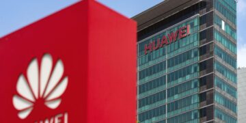 ساختمان اداری هواوی با لوگوی قرمز Huawei روی شیشهها و یک ماکت لوگوی بزرگ قرمز در پیشزمینه.