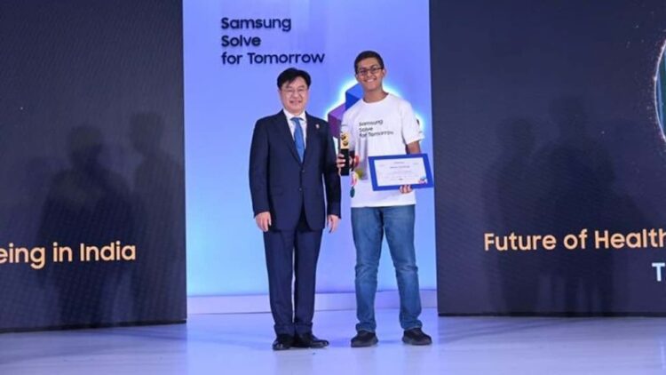 یک مرد کره‌ای با کت و شلوار در حال دادن گواهی یا جایزه به یک دانشجوی هندی که تی‌شرت آبی پوشیده، در مراسم "Samsung Solve for Tomorrow".