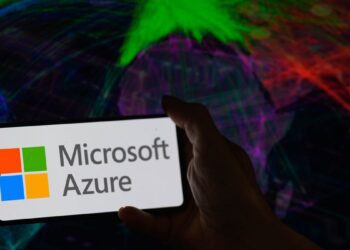 لوگوی Microsoft Azure روی صفحه یک گوشی هوشمند که توسط دست در مقابل یک پس‌زمینه رنگارنگ و انتزاعی از نور نگه داشته شده است.