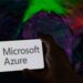 لوگوی Microsoft Azure روی صفحه یک گوشی هوشمند که توسط دست در مقابل یک پس‌زمینه رنگارنگ و انتزاعی از نور نگه داشته شده است.