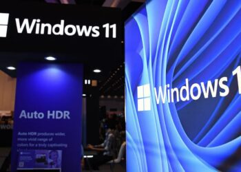 لوگوی Windows 11 در یک غرفه نمایشگاهی که قابلیت Auto HDR را برجسته می‌کند و یک نمایشگر بزرگ با طرح پس‌زمینه موج‌دار آبی Windows 11 در سمت راست دیده می‌شود.