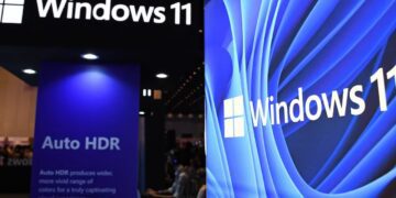 لوگوی Windows 11 در یک غرفه نمایشگاهی که قابلیت Auto HDR را برجسته می‌کند و یک نمایشگر بزرگ با طرح پس‌زمینه موج‌دار آبی Windows 11 در سمت راست دیده می‌شود.