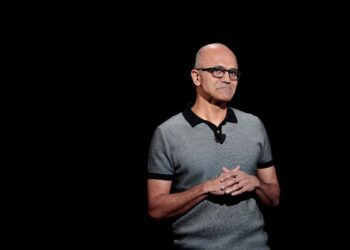 ساتیا نادلا (مدیرعامل مایکروسافت) با پیراهن پولو خاکستری در حال سخنرانی، با پس‌زمینه‌ای کاملاً مشکی.