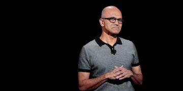 ساتیا نادلا (مدیرعامل مایکروسافت) با پیراهن پولو خاکستری در حال سخنرانی، با پس‌زمینه‌ای کاملاً مشکی.