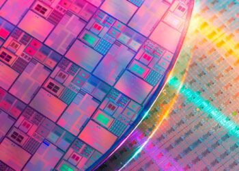 نمای نزدیک از یک ویفر سیلیکونی بزرگ با طراحیهای مدار میکروسکوپی در رنگهای متالیک روشن صورتی، آبی و نارنجی.