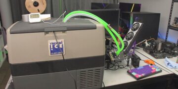 کارت گرافیک NVIDIA RTX 5050 که به یک بلوک خنککننده آب متصل شده است و لولههای سبز فلورسنت مایع خنککننده از آن به یک فریزر کمپینگ Tecni Ice متصل شدهاند، در یک محیط دسکتاپ.
