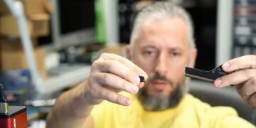 یک مرد ریشو که قطعه شکسته یک کانکتور کارت گرافیک را در یک دست و بخش اصلی کانکتور را در دست دیگر گرفته است.