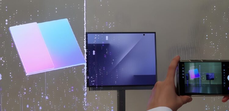 نمایشگر تاشو سامسونگ که یک مکعب سه‌لته‌ای رنگارنگ (صورتی و آبی) را نمایش می‌دهد و یک فرد با گوشی خود در حال عکاسی از آن است.