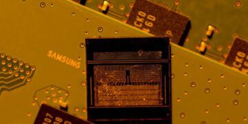 نمای نزدیک از یک تراشه حافظه با بافت داخلی قابل مشاهده، که روی یک برد مدار چاپی (PCB) زرد/زیتونی قرار دارد و لوگوی "SAMSUNG" روی برد دیده میشود.