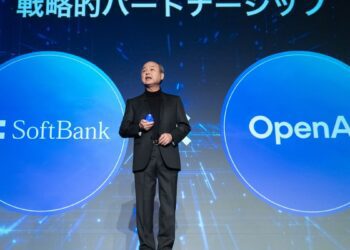 ماسایوشی سان، مدیرعامل سافت‌بانک، با کت و شلوار در حال سخنرانی روی صحنه، که در دو طرف او دایره‌های بزرگ آبی با لوگوی "SoftBank" و "OpenAI" نمایش داده شده است.