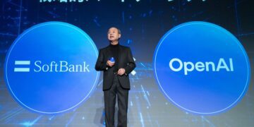 ماسایوشی سان، مدیرعامل سافت‌بانک، با کت و شلوار در حال سخنرانی روی صحنه، که در دو طرف او دایره‌های بزرگ آبی با لوگوی "SoftBank" و "OpenAI" نمایش داده شده است.