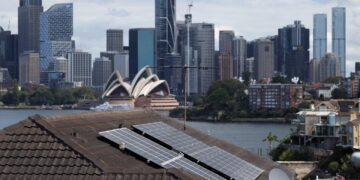 نمایی از بام خانهای با پنلهای خورشیدی در سیدنی، با پسزمینهای از ساختمان اپرای معروف و برجهای مرکز شهر.
