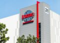 نمای بیرونی یک ساختمان TSMC با لوگوی قرمز رنگ شرکت، یک نوار عمودی قرمز و عدد "21" در گوشه ساختمان.