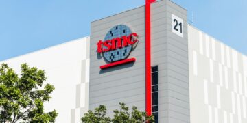 نمای بیرونی یک ساختمان TSMC با لوگوی قرمز رنگ شرکت، یک نوار عمودی قرمز و عدد "21" در گوشه ساختمان.