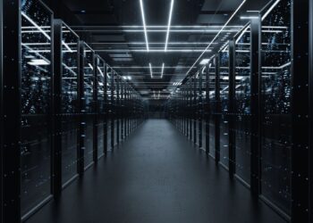 یک راهرو طولانی و تاریک در یک مرکز داده (Data Center) با ردیف‌هایی از رک‌های سرور روشن با نورهای آبی نئونی.