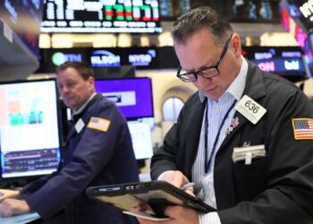 یک کارگزار بورس (Stock Broker) در طبقه بورس نیویورک (NYSE) در حال بررسی داده‌ها روی یک تبلت.