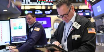 یک کارگزار بورس (Stock Broker) در طبقه بورس نیویورک (NYSE) در حال بررسی داده‌ها روی یک تبلت.