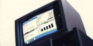 یک کامپیوتر قدیمی با مانیتور CRT که رابط کاربری گرافیکی ویندوز ۱.۰۱ را نمایش می‌دهد و برنامه‌هایی مانند Microsoft Multiplan و یک چارت نواری در آن دیده می‌شود.