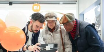 یک کارمند شیائومی در حال کمک به دو فرد مسن برای استفاده از یک تبلت با کیبورد در داخل فروشگاه شیائومی در پاریس.