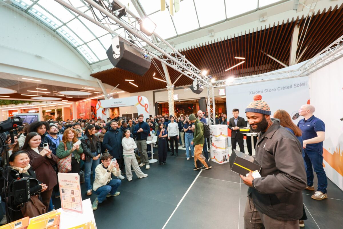 یک صحنه شلوغ در داخل یک مرکز خرید در افتتاحیه فروشگاه شیائومی در فرانسه، با حضور یک مجری و جمعیت زیاد.