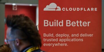 یک بنر تبلیغاتی Cloudflare با لوگوی سفید و شعار "Build Better" که در یک رویداد یا کنفرانس دیده میشود.