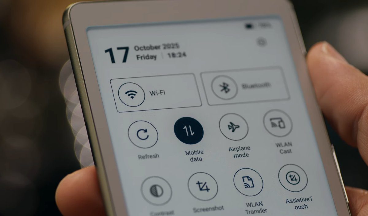 نمای نزدیک از یک دست که یک دستگاه مطالعه الکترونیکی (e-reader) را نگه داشته و صفحه نمایش آن بخش تنظیمات سریع (Quick Settings) را با آیکون‌هایی مانند Wi-Fi، Bluetooth و Mobile data نشان می‌دهد.