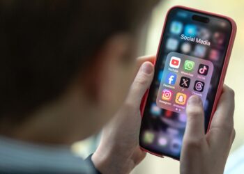 تصویری از آیکون برنامه‌های شبکه‌های اجتماعی روی یک گوشی در دست‌های یک کودک