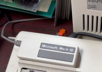 نمای نزدیک از دستگاه خارجی "Microsoft Mach 10" با کابلهای متصل، که در کنار یک واحد کامپیوتر قدیمی IBM Personal Computer XT قرار دارد.