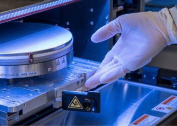 تراشهٔ سیلیکونی درون دستگاه ساخت نیمههادی، هنگام نصب و بررسی معماری سهبعدی با دستکش ایمنی در محیط آزمایشگاهی.