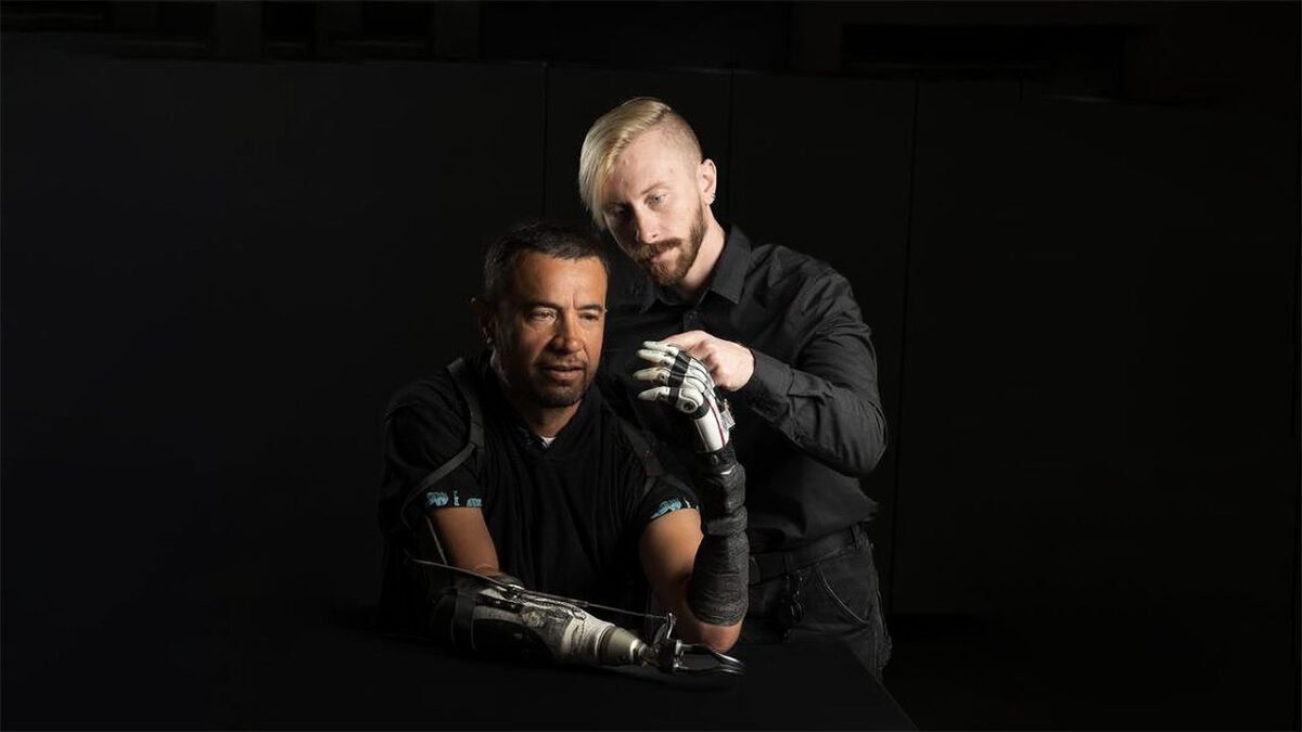 یک پژوهشگر در حال تنظیم و آموزش دست بیونیک یک مرد دارای قطع عضو؛ تصویر نمایانگر آزمایش و کنترل یک پروتز پیشرفته با حسگرهای حرکتی و لمس مصنوعی