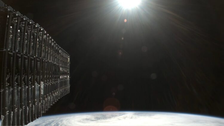 نمای نزدیک از مجموعه ماهوارههای Starlink متصلبههم در مدار پایین زمین، با پسزمینه انحنای زمین و تابش نور خورشید، نماد توسعه اینترنت ماهوارهای اسپیسایکس