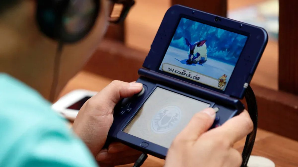 نمای نزدیک از کنسول دستی Nintendo 3DS در حال اجرا یک بازی ویدیویی، با نمایش صحنه گیم‌پلی روی صفحه بالا و کنترل دستگاه توسط دست‌ها