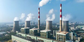 نمای هوایی نیروگاه حرارتی با چهار برج خنک‌کن و دودکش اصلی، انتشار بخار آب به آسمان و قرارگیری تاسیسات صنعتی در حاشیه شهر