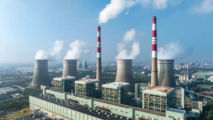 نمای هوایی نیروگاه حرارتی با چهار برج خنک‌کن و دودکش اصلی، انتشار بخار آب به آسمان و قرارگیری تاسیسات صنعتی در حاشیه شهر