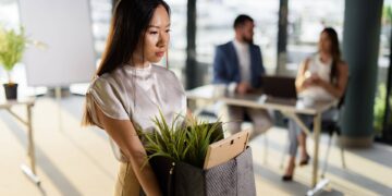 زنی با چهره‌ای غمگین در حال حمل جعبه وسایل شخصی خود پس از اخراج از محیط کار.