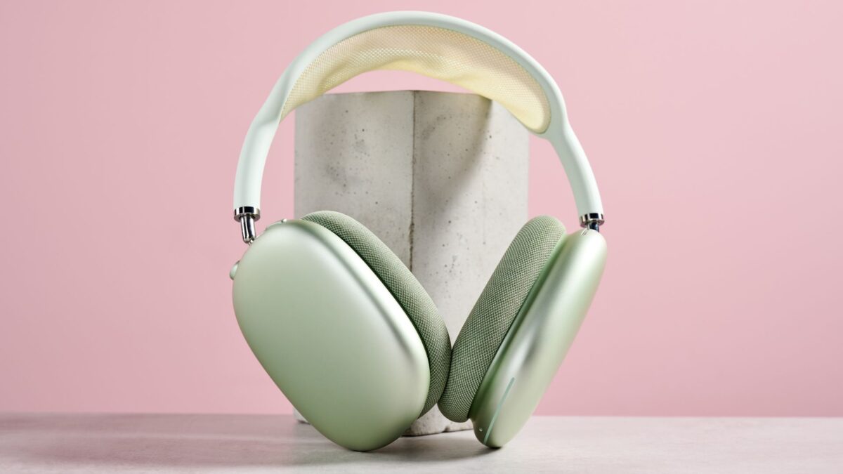 هدفون AirPods Max سبز رنگ که روی یک مکعب بتنی در پسزمینه صورتی قرار دارد.