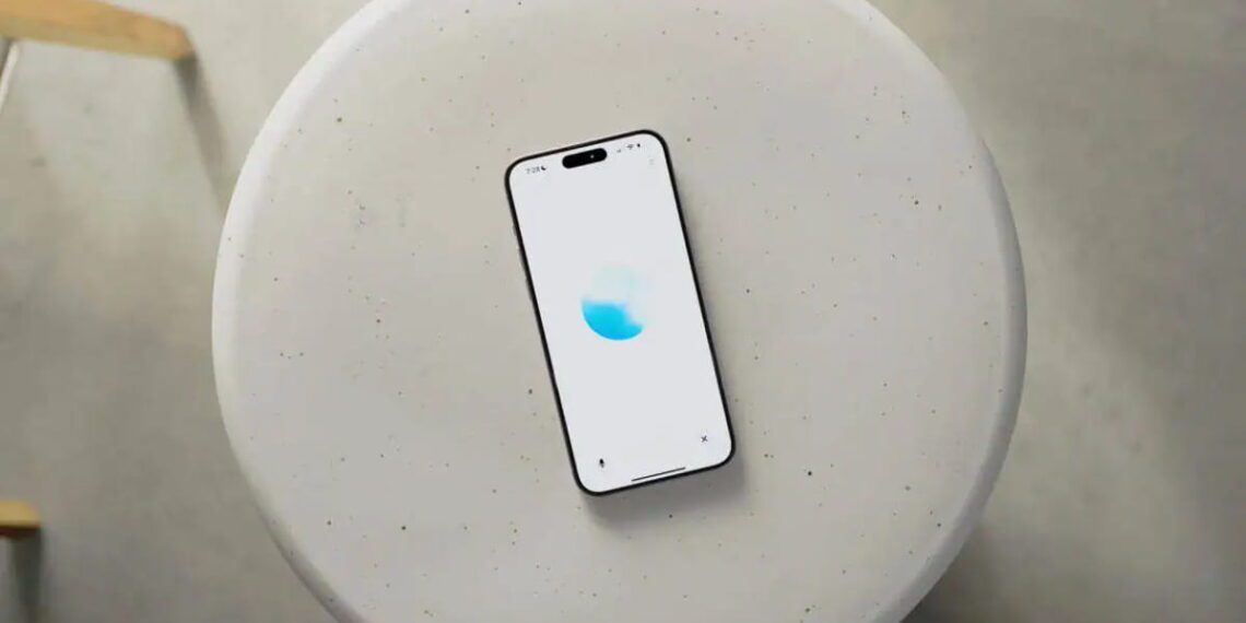 نمای بالاسری از یک گوشی هوشمند قرارگرفته روی میز گرد روشن با رابط کاربری ChatGPT Voice، نمایش انیمیشن صوتی آبی‌رنگ و اشاره به قابلیت مکالمه صوتی پیشرفته هوش مصنوعی