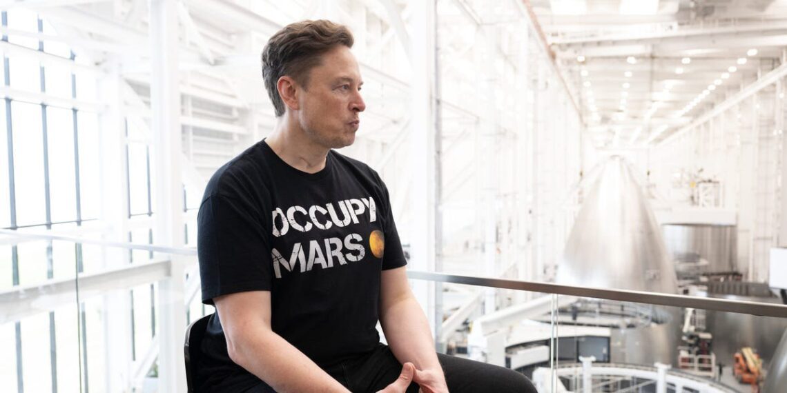 ایلان ماسک با تی‌شرت مشکی "Occupy Mars" در حال نشستن در داخل یکی از سوله‌های صنعتی اسپیس‌اکس.